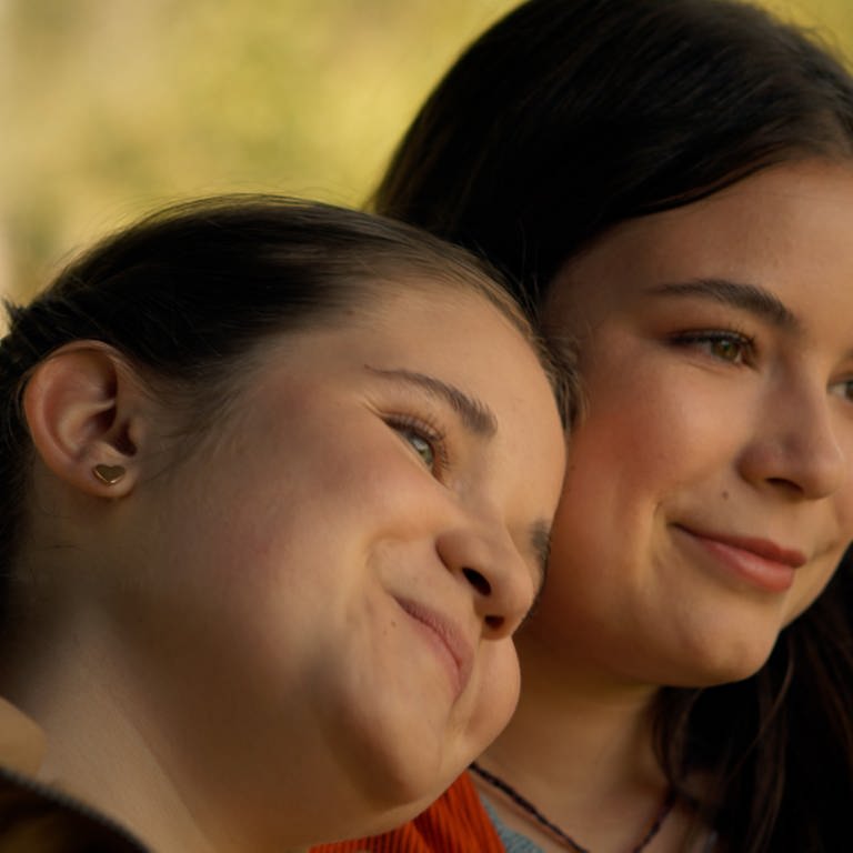 Zwei Mädchen lehnen ihre Köpfe aneinander und lächeln glücklich