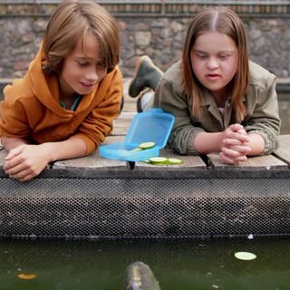 Ein Junge und ein Mädchen liegen auf einem Steg ins Wasser schauend
