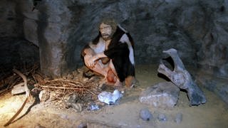 Eine Neanderthaler-Nachbildung in einer Höhle neben einer Feuerstelle
