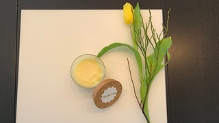 Ein Tigel mit Handcreme steht auf einem Tisch, eine gelbe Tulpe liegt daneben